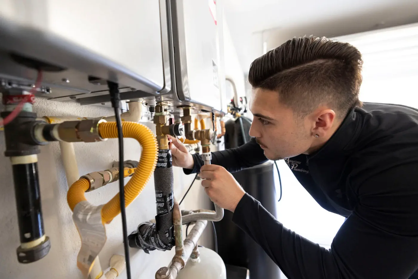 A plumber checking the gas and water connections on a wall-mounted tankless water heater