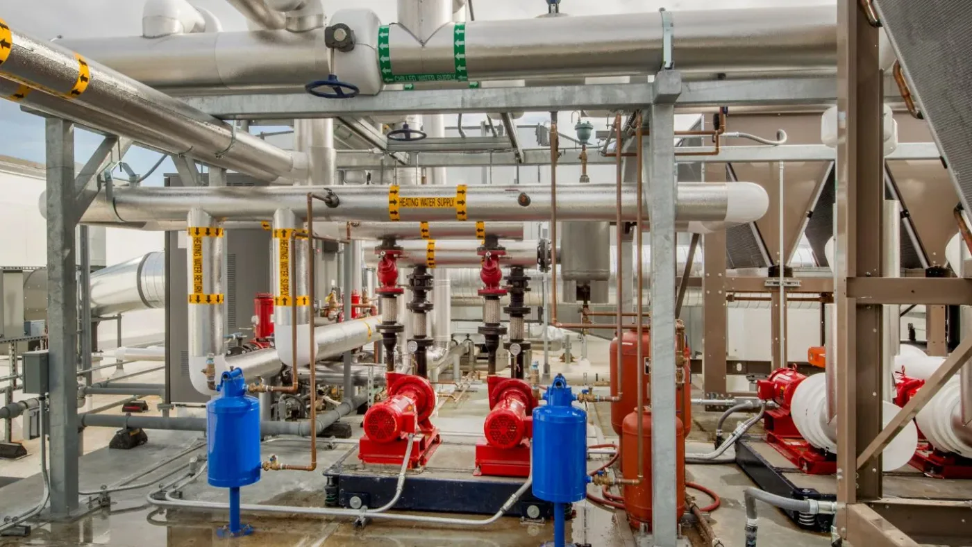 Color-coded heating and chilled-water mains feeding circulation pumps in a mechanical plant — plumbing contractor insurance in Tennessee