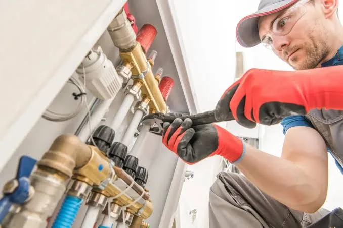 A plumber in work gloves adjusting a fitting on a color-coded water manifold — plumbing contractor insurance in Florida