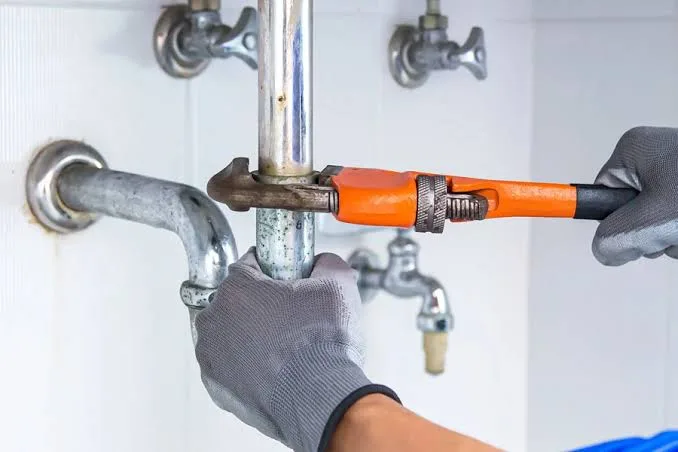 A plumber using a pipe wrench on a galvanized supply line and shutoff valve under a sink — plumbing contractor insurance in New Jersey